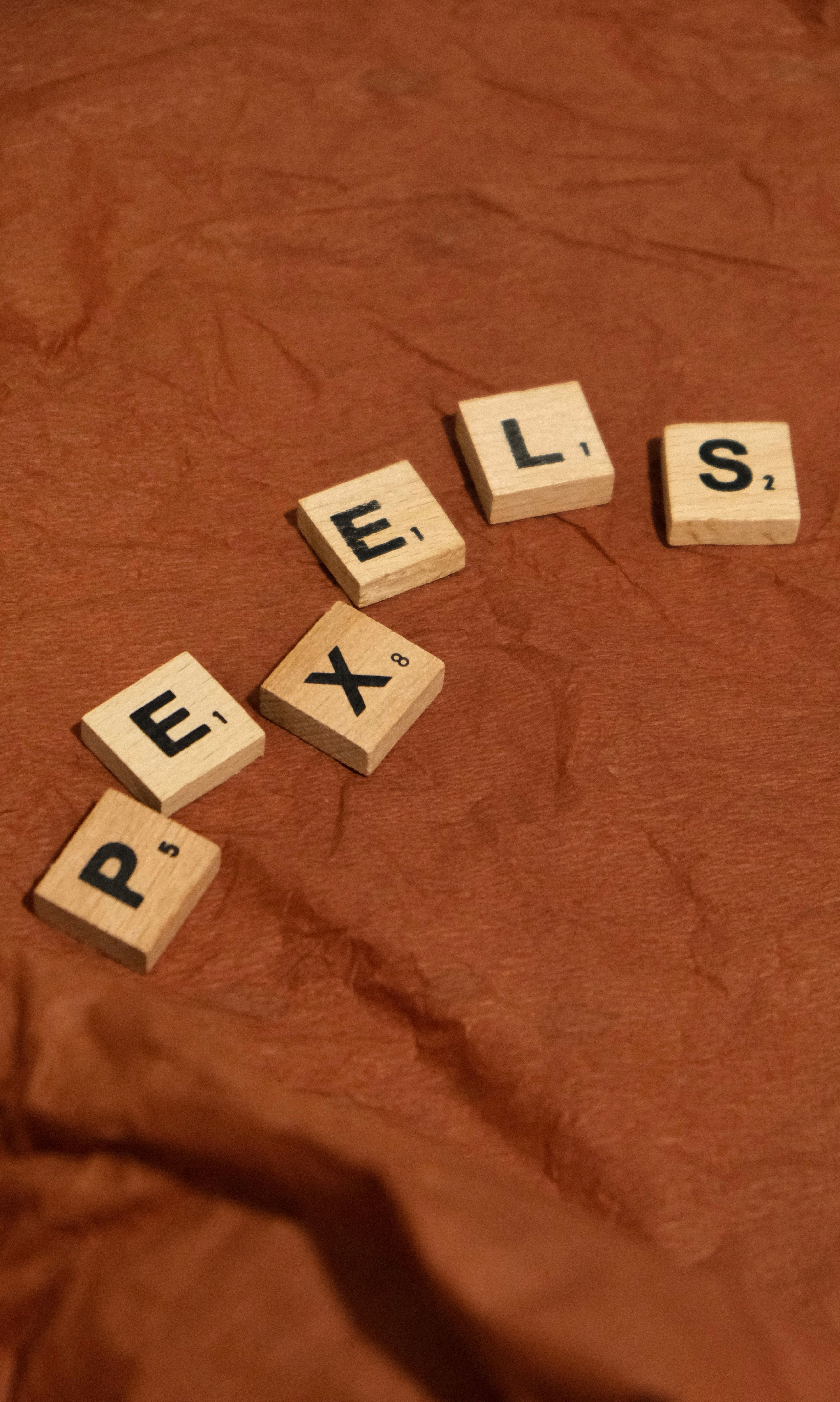 Wooden letter tiles spelling 'PEXELS' on a textured brown fabric background.