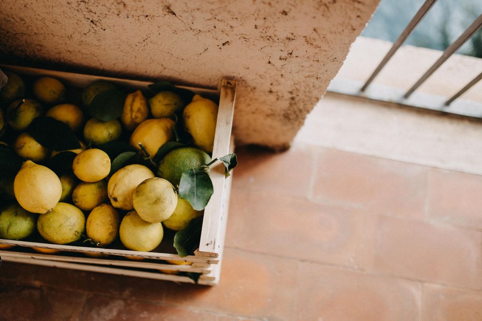 A rustic wooden crate filled with fresh lemons and leaves, captured in an outdoor setting.