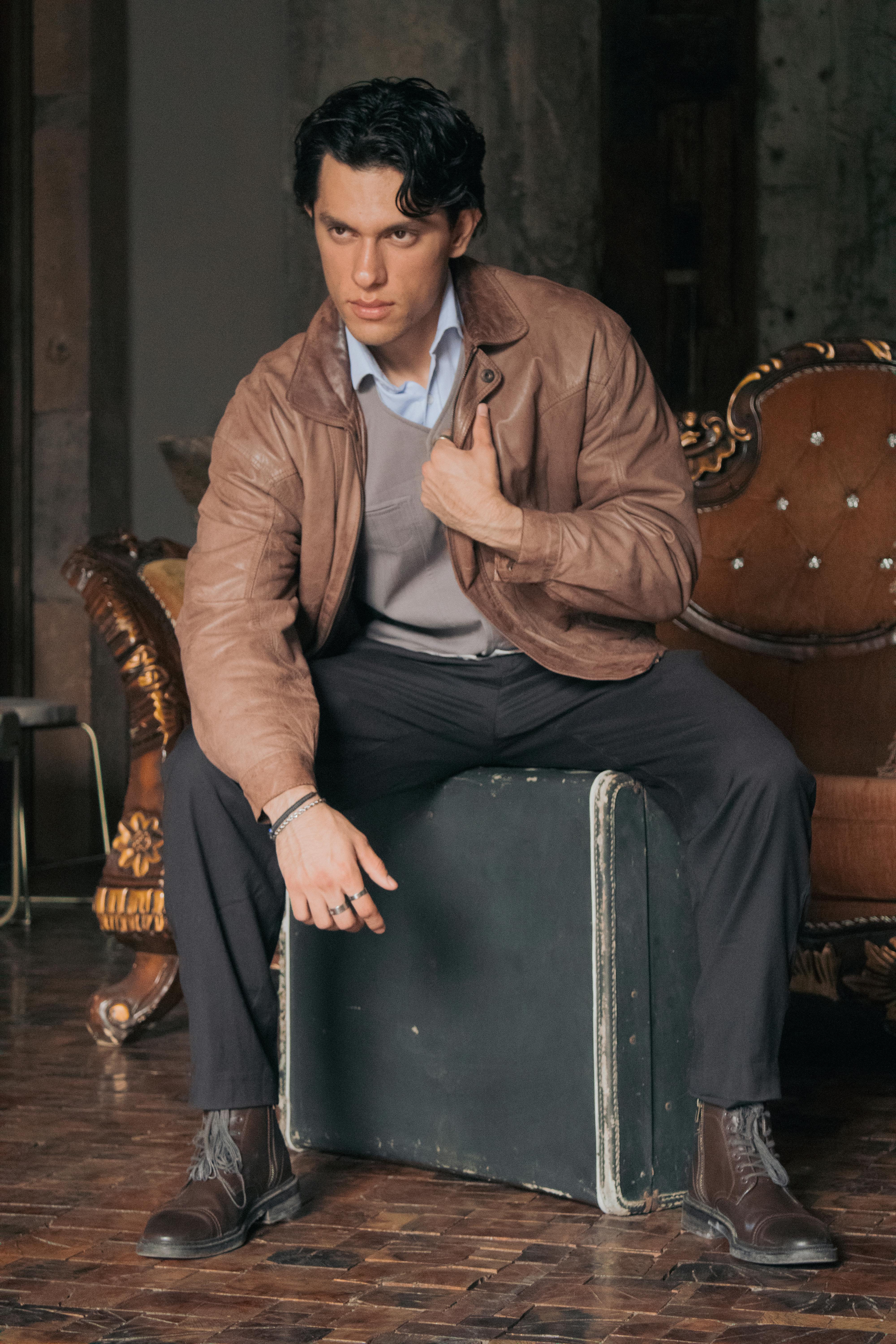 a man in a leather jacket sitting on a suitcase