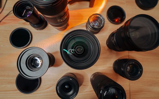 Top view of various camera lenses and caps on a wooden floor, ideal for photography and tech content.