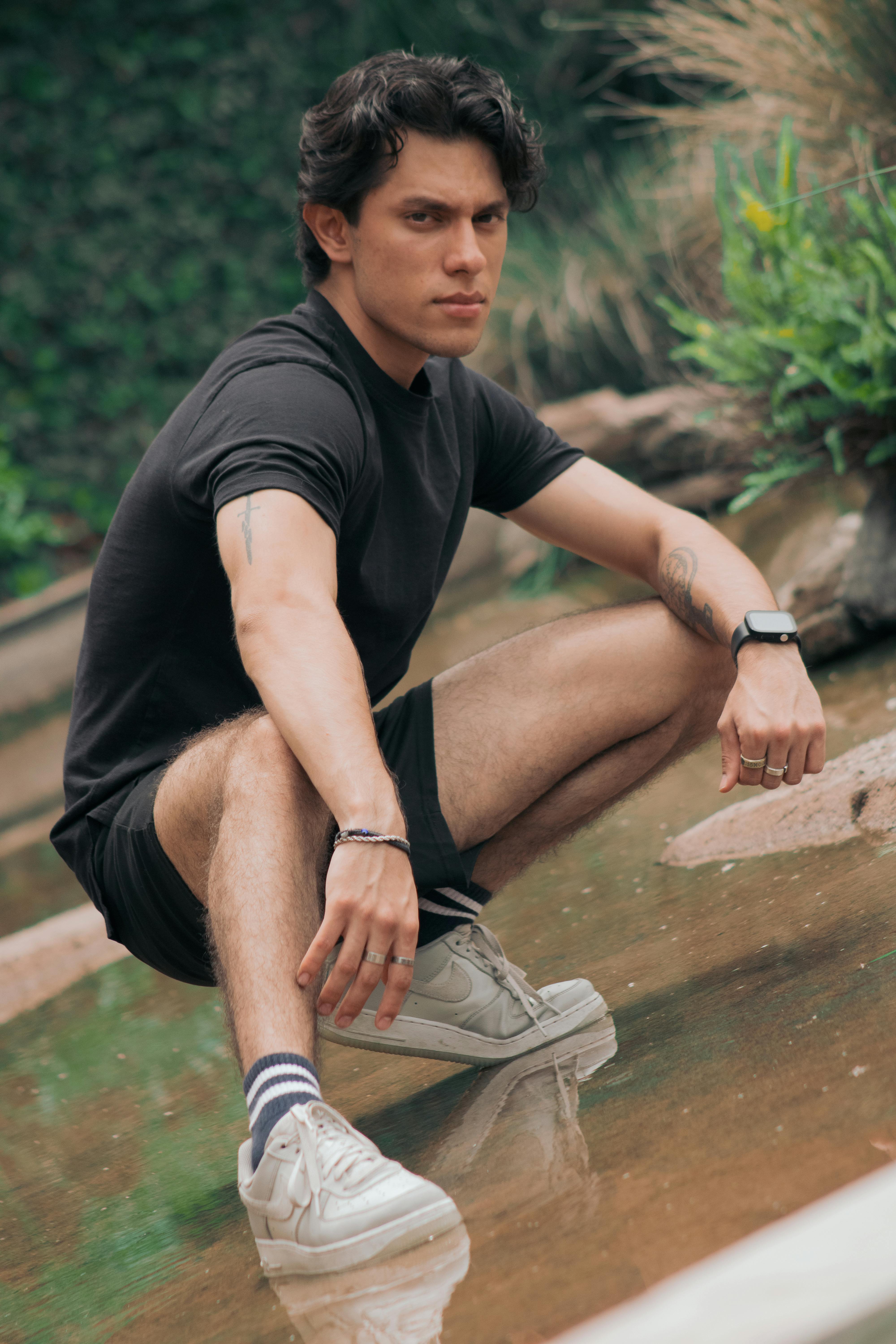 a man in black shirt and sneakers crouches down in a pond