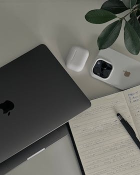 Flat lay of a modern workspace with Apple devices, notebook, and pen highlighting productivity.