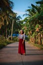一位身着红色连衣裙的时尚女子在郁郁葱葱的热带风景中摆姿势