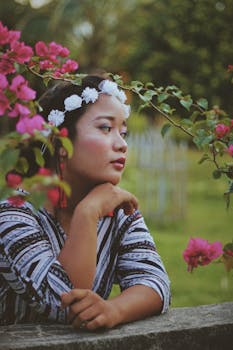 一位头戴花冠的女子，在户外的九重葛丛中若有所思地摆着姿势