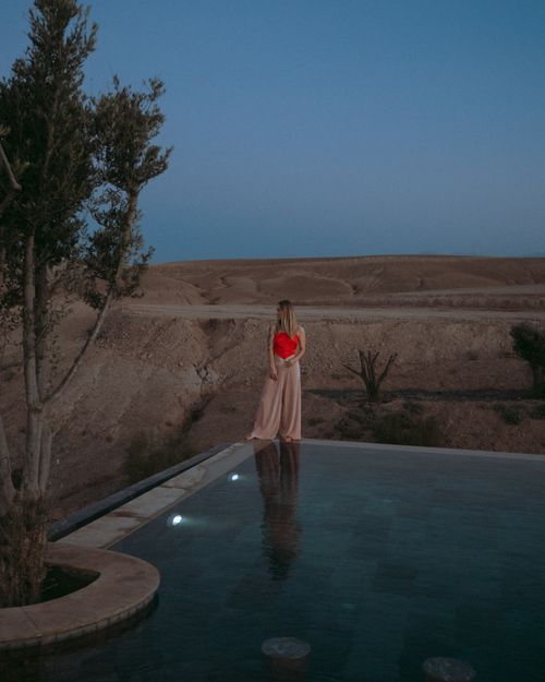 Free A woman in a vibrant dress standing by an infinity pool in the Agafay Desert, Morocco. Stock Photo