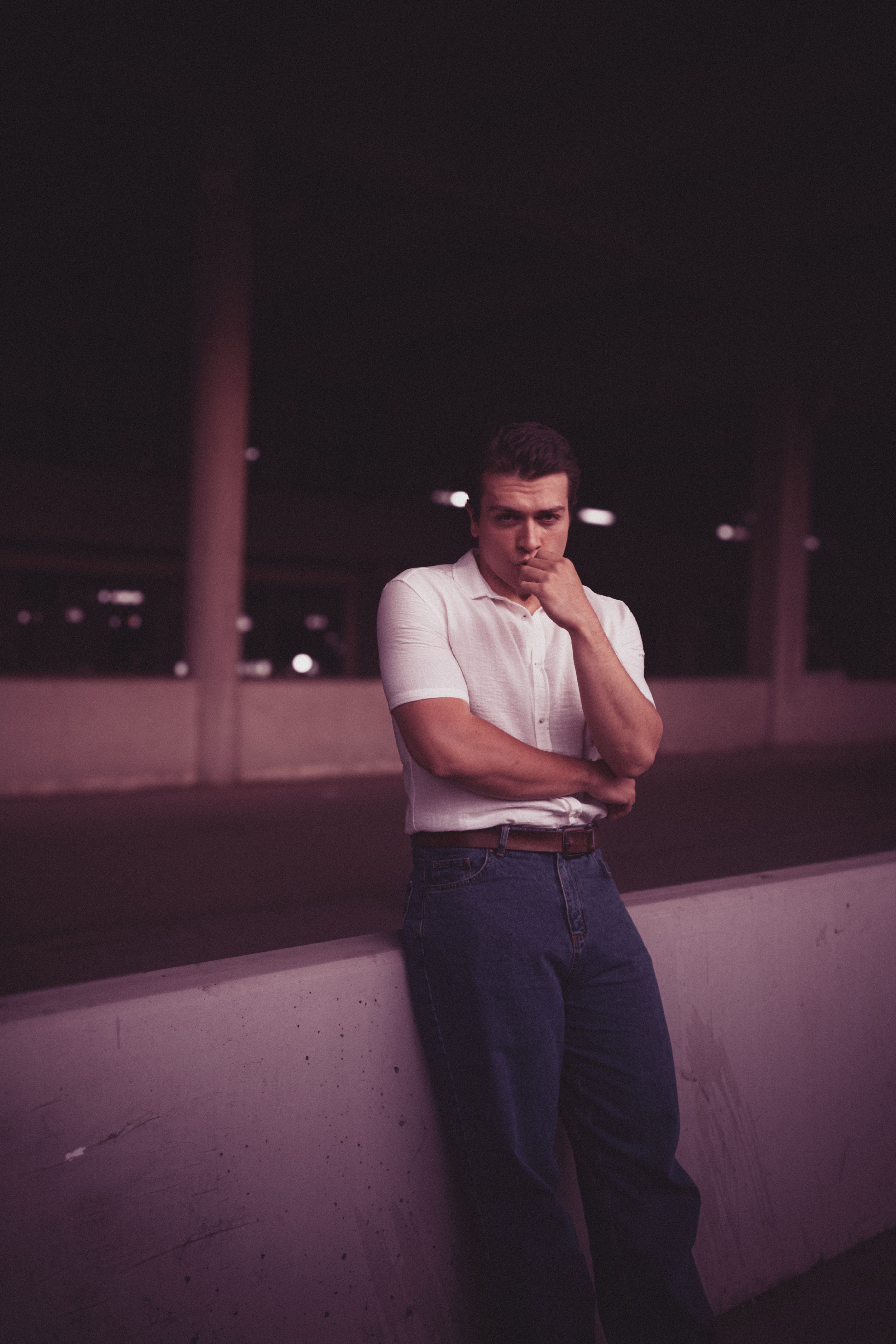 A man in a white shirt and jeans leaning against a wall · Free Stock Photo