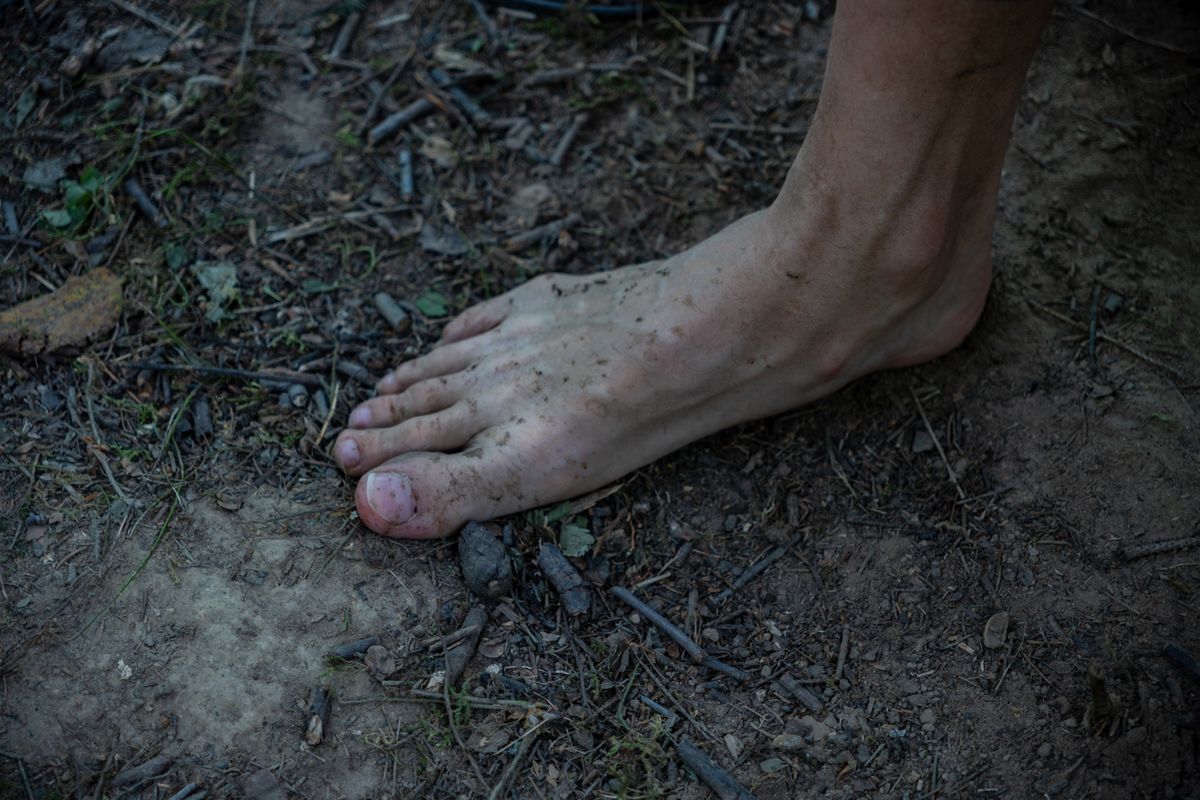 Bare feet resting on damp earth and fallen leaves in a forest, representing grounding practice