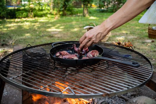 A vibrant outdoor grilling scene with octopus being prepared in a pan over an open flame.