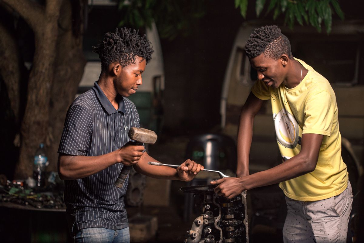 Two mechanics repairing a car engine outdoors