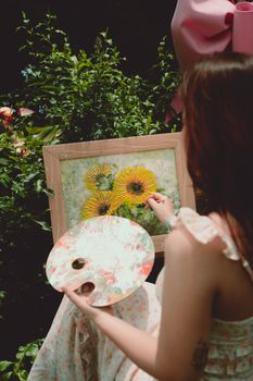 A woman artist painting sunflowers outdoors surrounded by greenery.