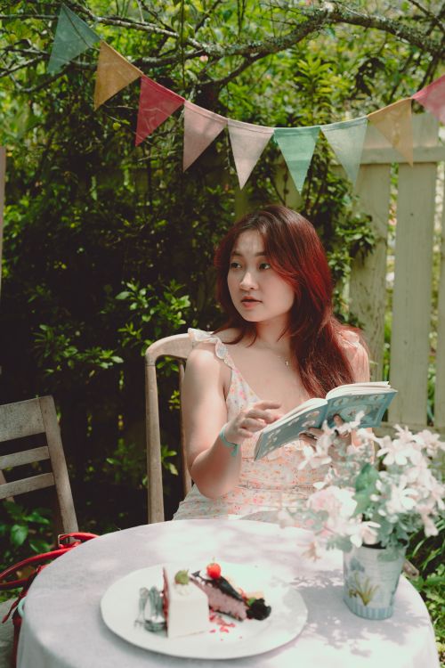 Free A young woman enjoys reading outdoors with cake and festive decor. Stock Photo