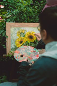Person painting vibrant sunflowers on canvas in a lush green garden. Artistic scene.