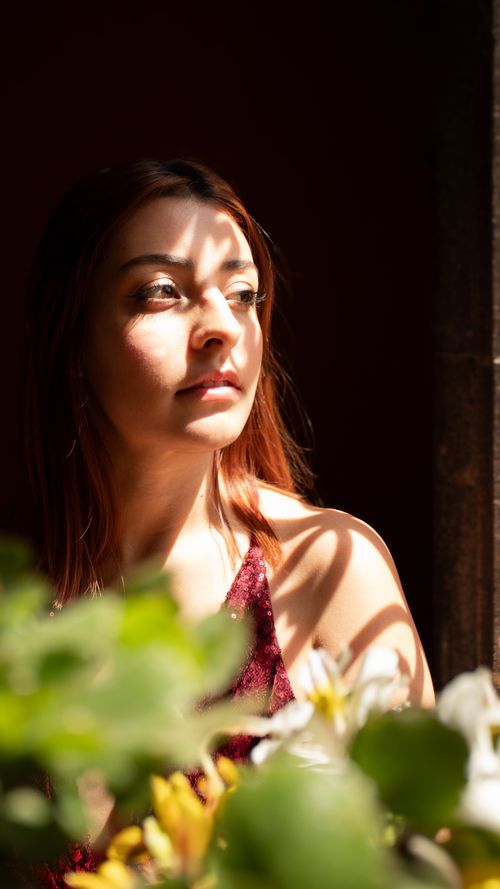 Free A thoughtful woman in natural light, surrounded by flowers, casting shadows over her face. Stock Photo