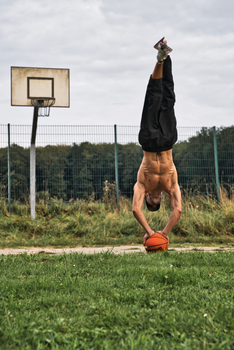 An athletic man performs a handstand on a basketball outdoors, showcasing impressive strength and balance.