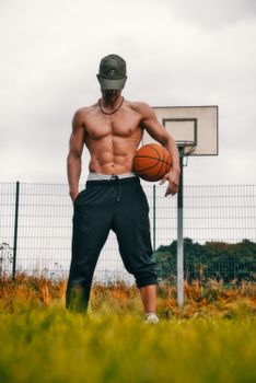 Young man displaying muscles with basketball on outdoor court, fitness themed.