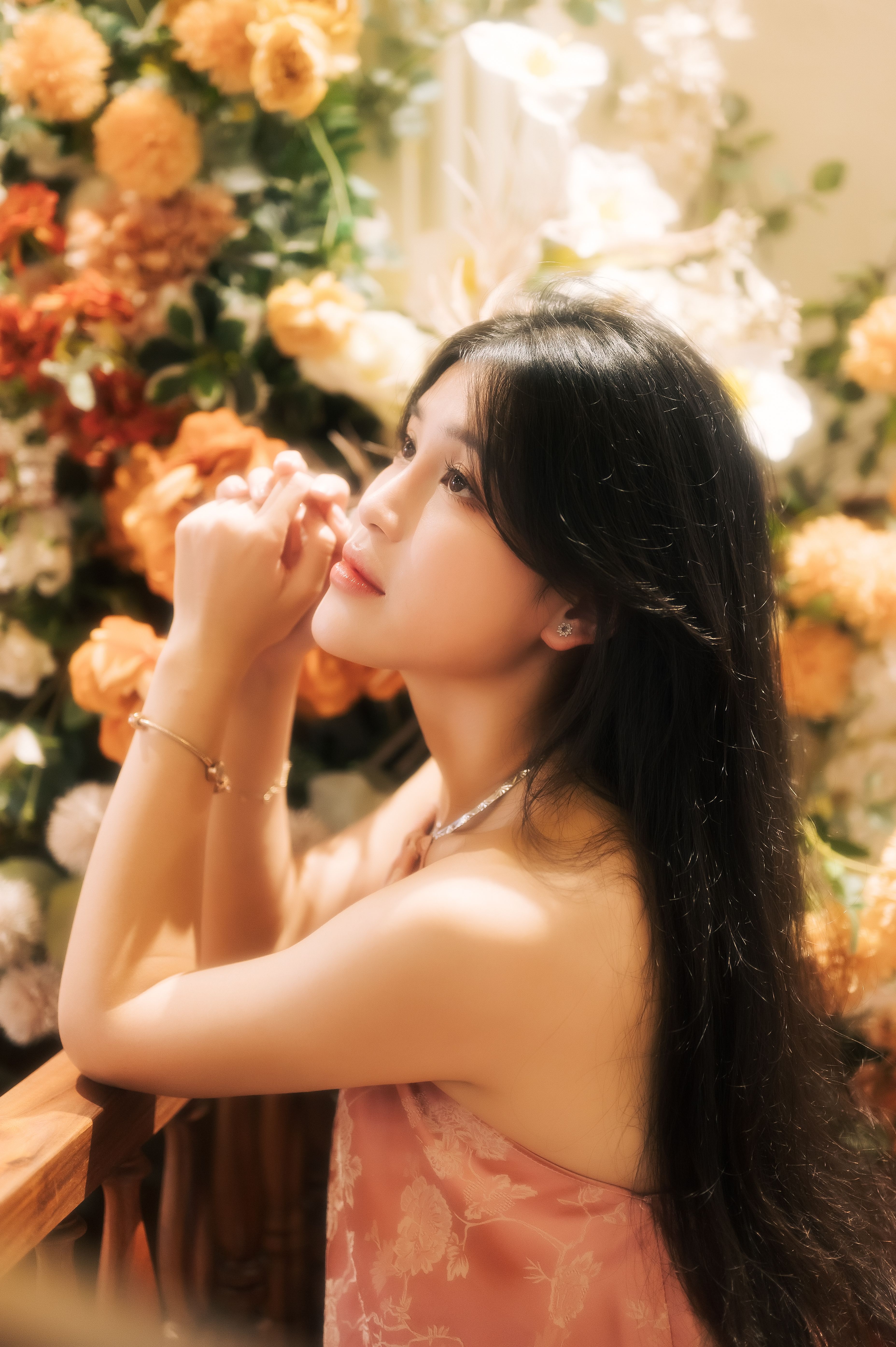 A beautiful woman surrounded by vibrant flowers in a contemplative pose.