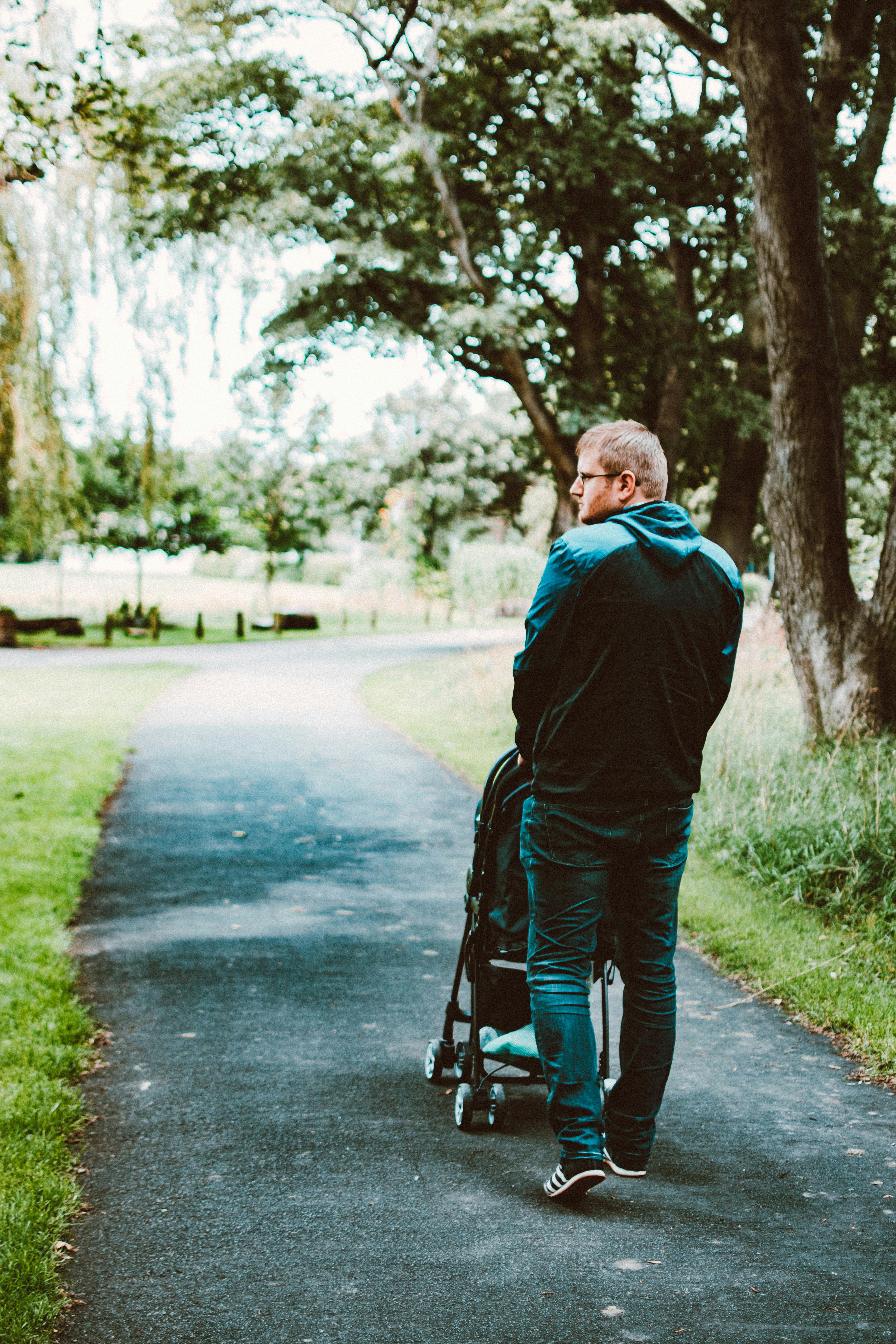 一名成年男子推着婴儿车，在绿树成荫的公园小路上漫步