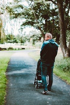 一名成年男子推着婴儿车，在绿树成荫的公园小路上漫步