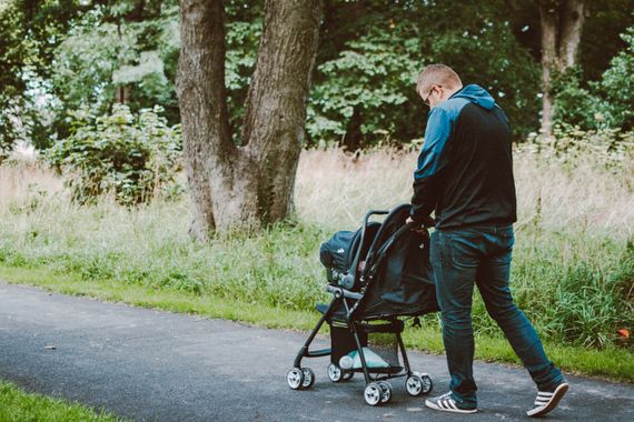 A parent pushing a stroller along a green park pathway