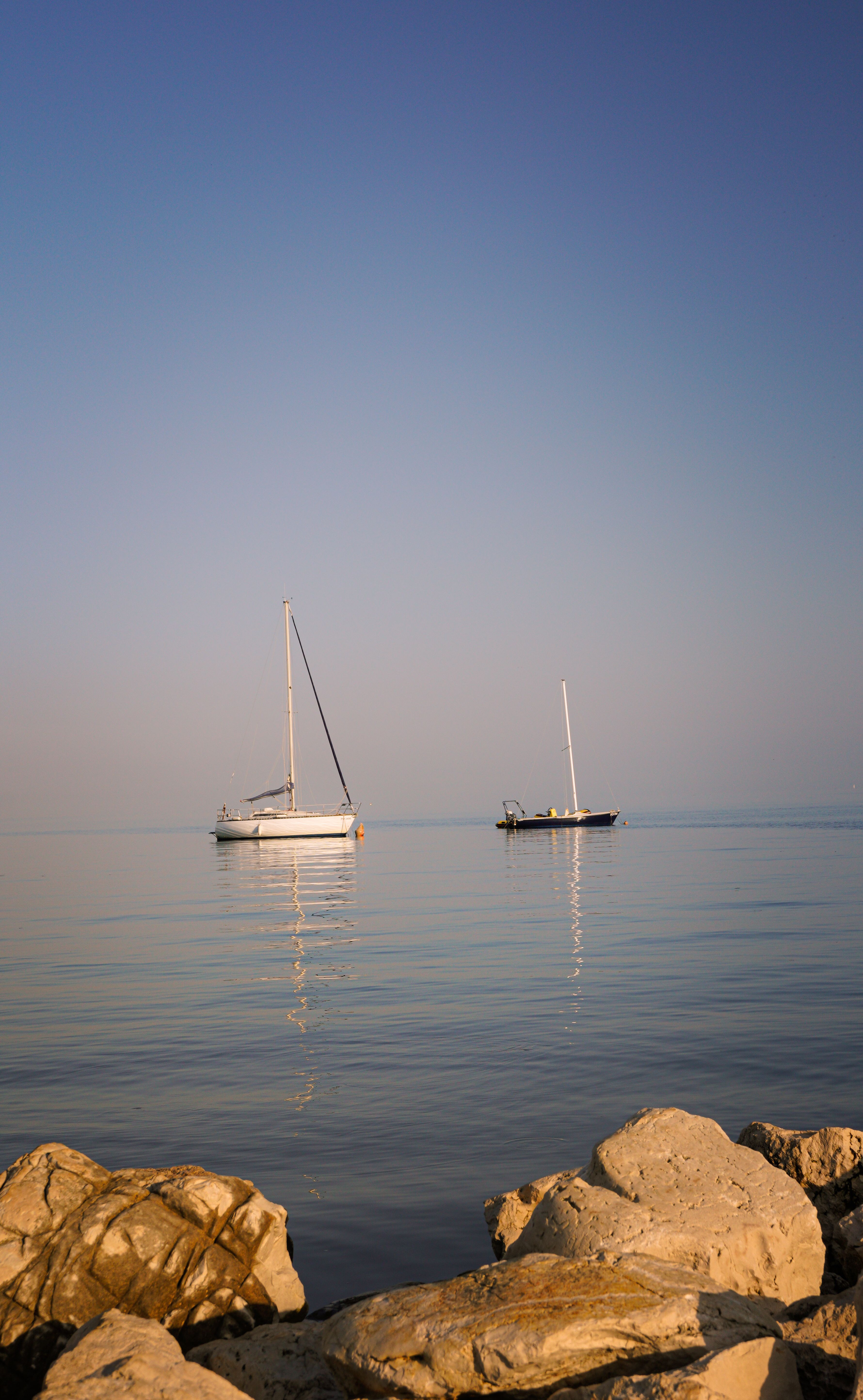 Two sailboats are anchored in the water near rocks · Free Stock Photo