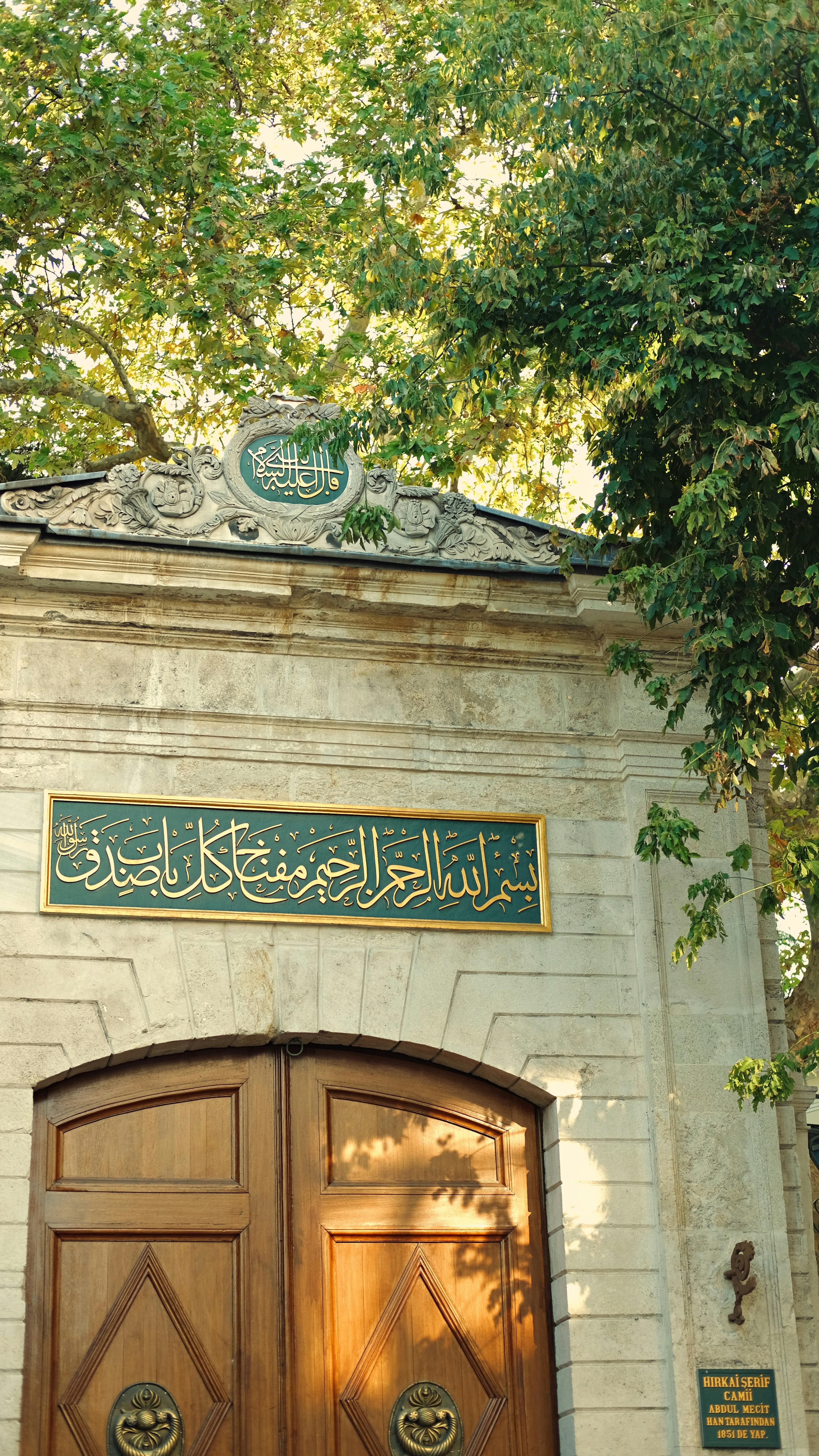 Elegant wooden door adorned with Arabic calligraphy under a lush green foliage, capturing a serene outdoor ambiance.