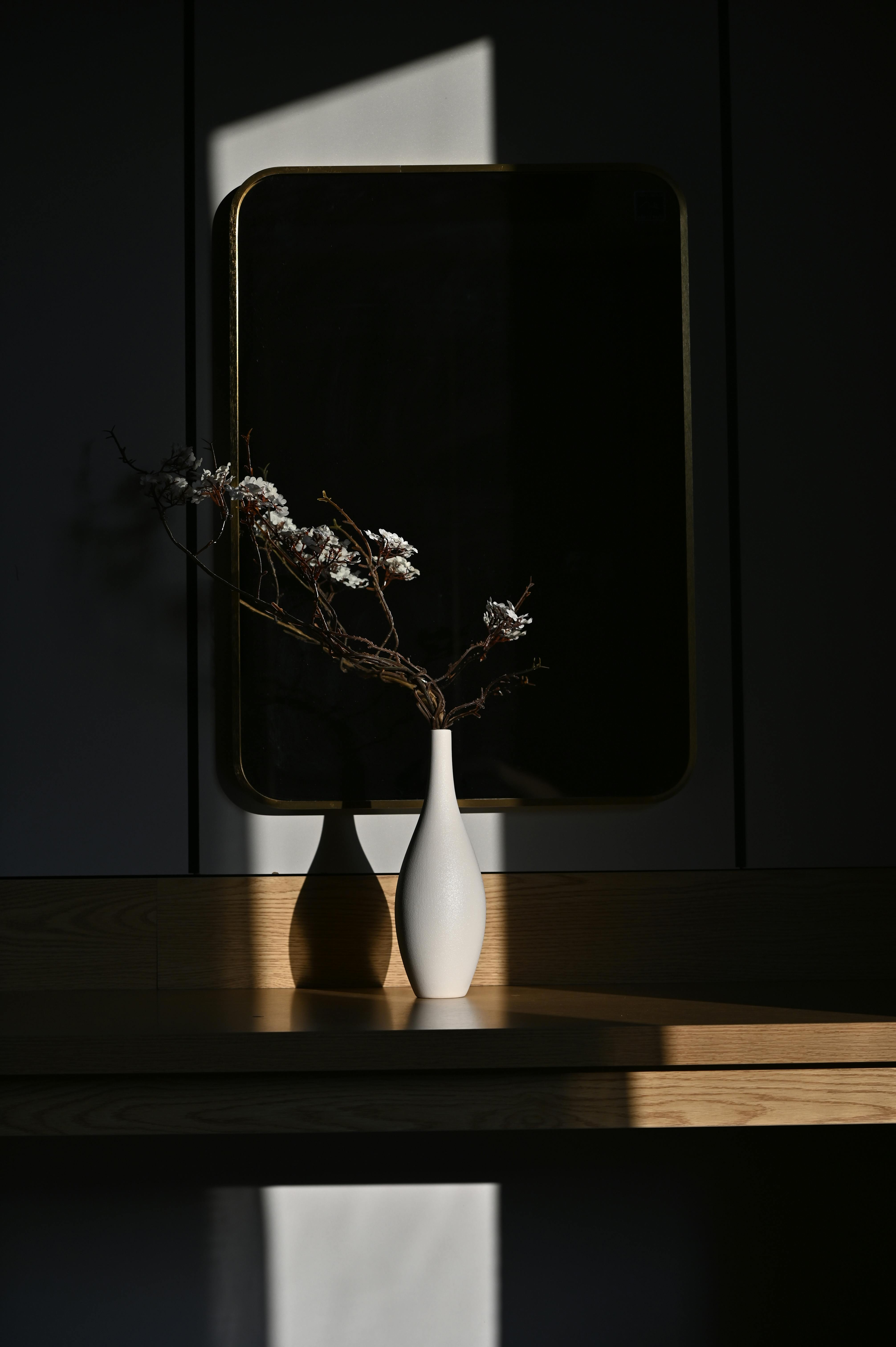 Minimalist still life of a white vase with flowers casting shadows in soft light.