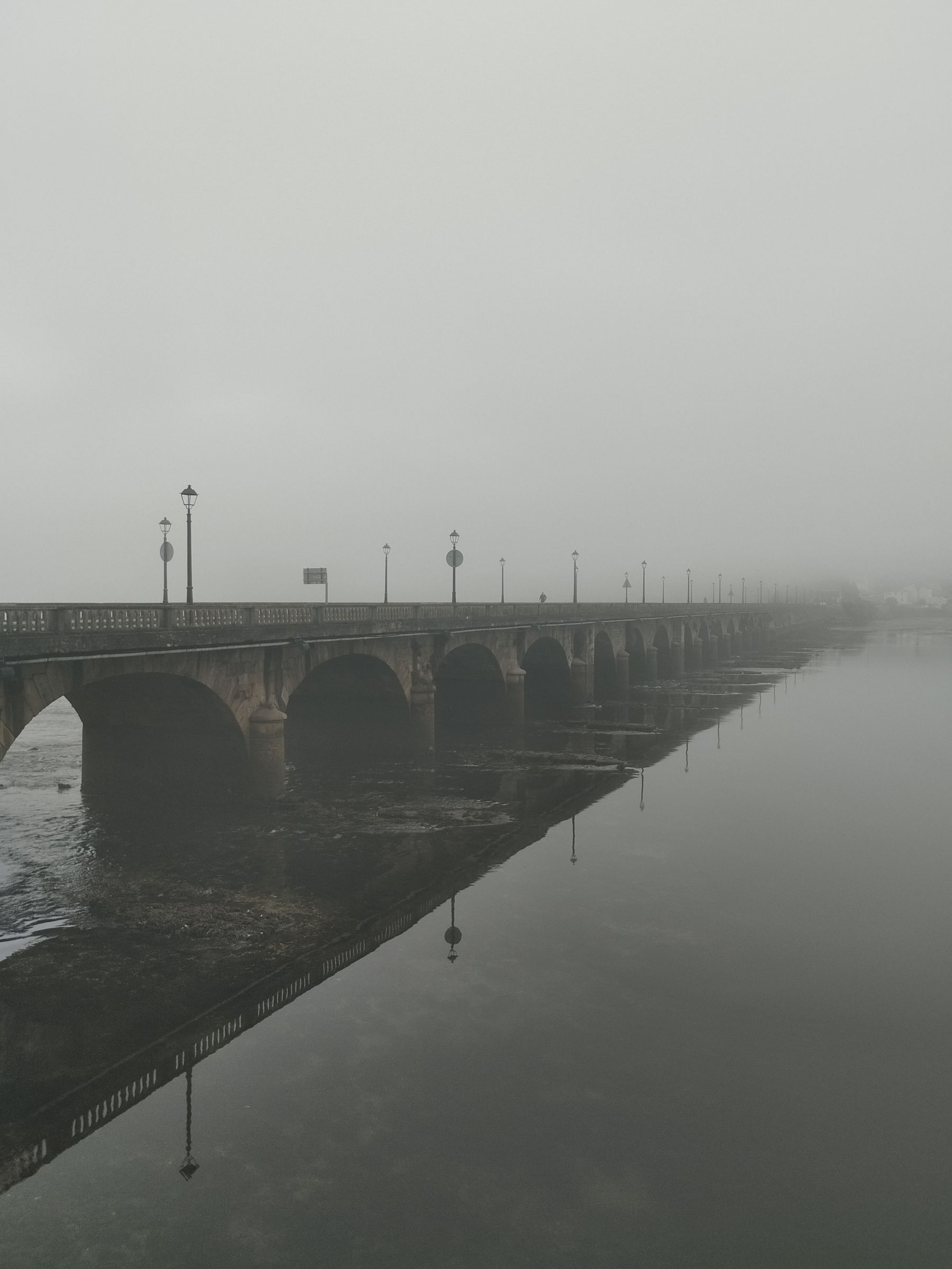 A stone bridge reflected in still water at dawn, mist over the surface