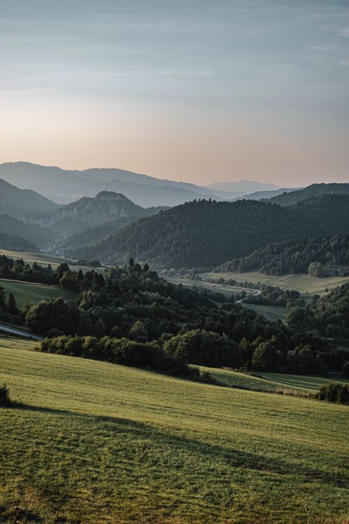 Free Serene view of a lush green valley with rolling hills and mountains under a soft evening sky. Stock Photo