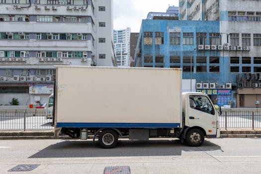 A delivery truck parked on a city street against a backdrop of urban buildings.