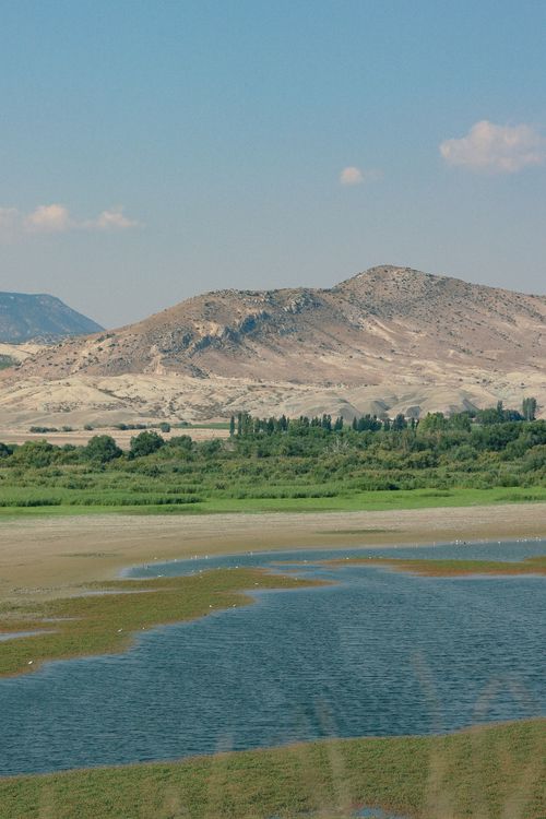Free Picturesque landscape of a serene lake surrounded by green valley and mountains under a clear sky. Stock Photo