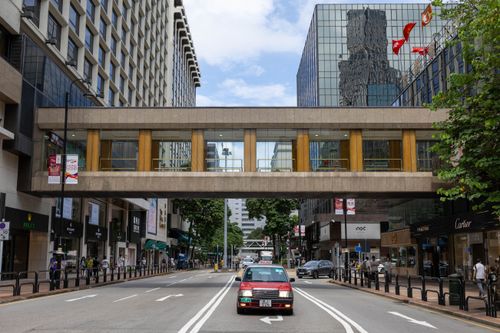 Free Bustling city street featuring a pedestrian bridge, modern architecture, and a red taxi driving below. Stock Photo