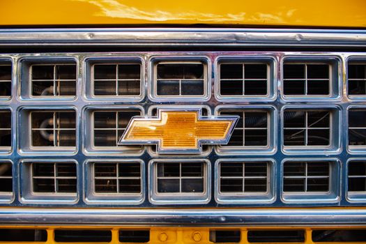 Front grille of a classic yellow Chevrolet truck highlighting chrome details.