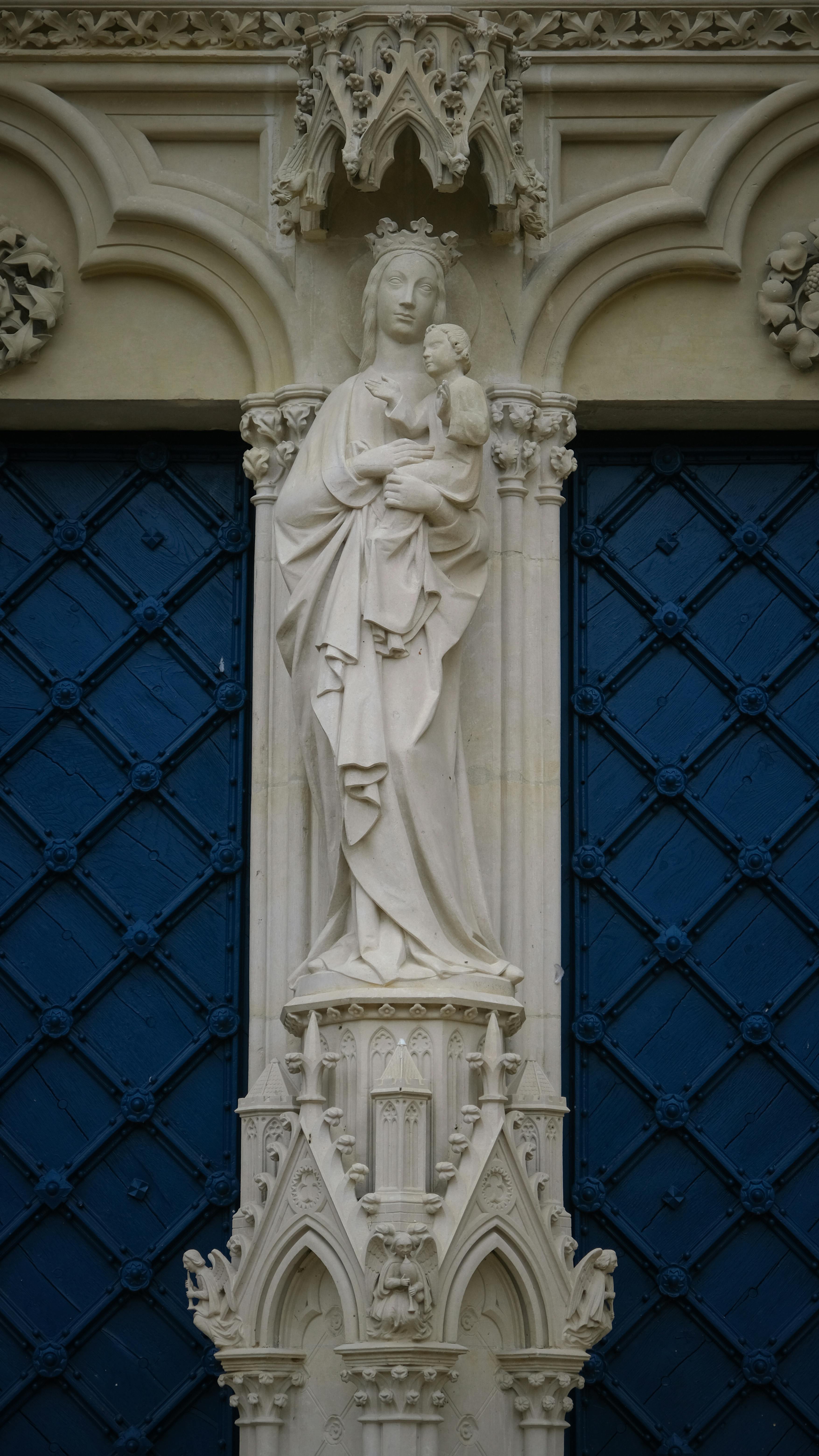 Intricate gothic sculpture of Virgin Mary and Child on blue church door.