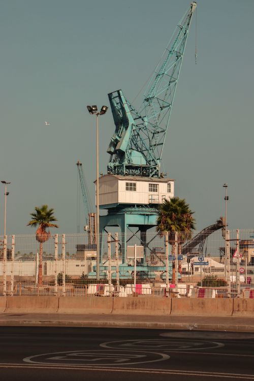 Free A large harbor crane stands prominently in an outdoor industrial area under a clear sky. Stock Photo
