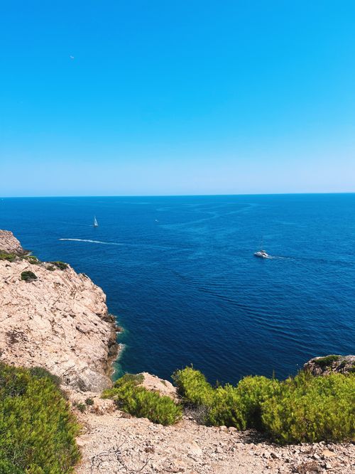 Free Breathtaking view of a rocky coastline and boats sailing under a clear blue sky. Stock Photo