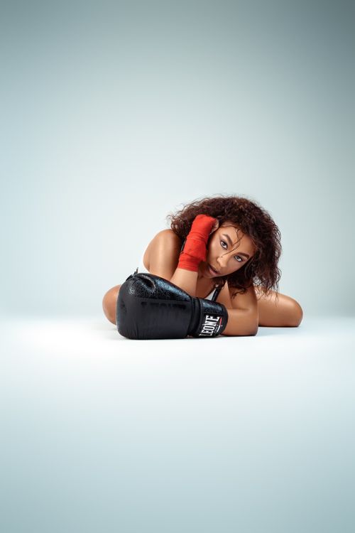 Free Portrait of a young female boxer in a studio setting with boxing gloves and red wrist wraps. Stock Photo