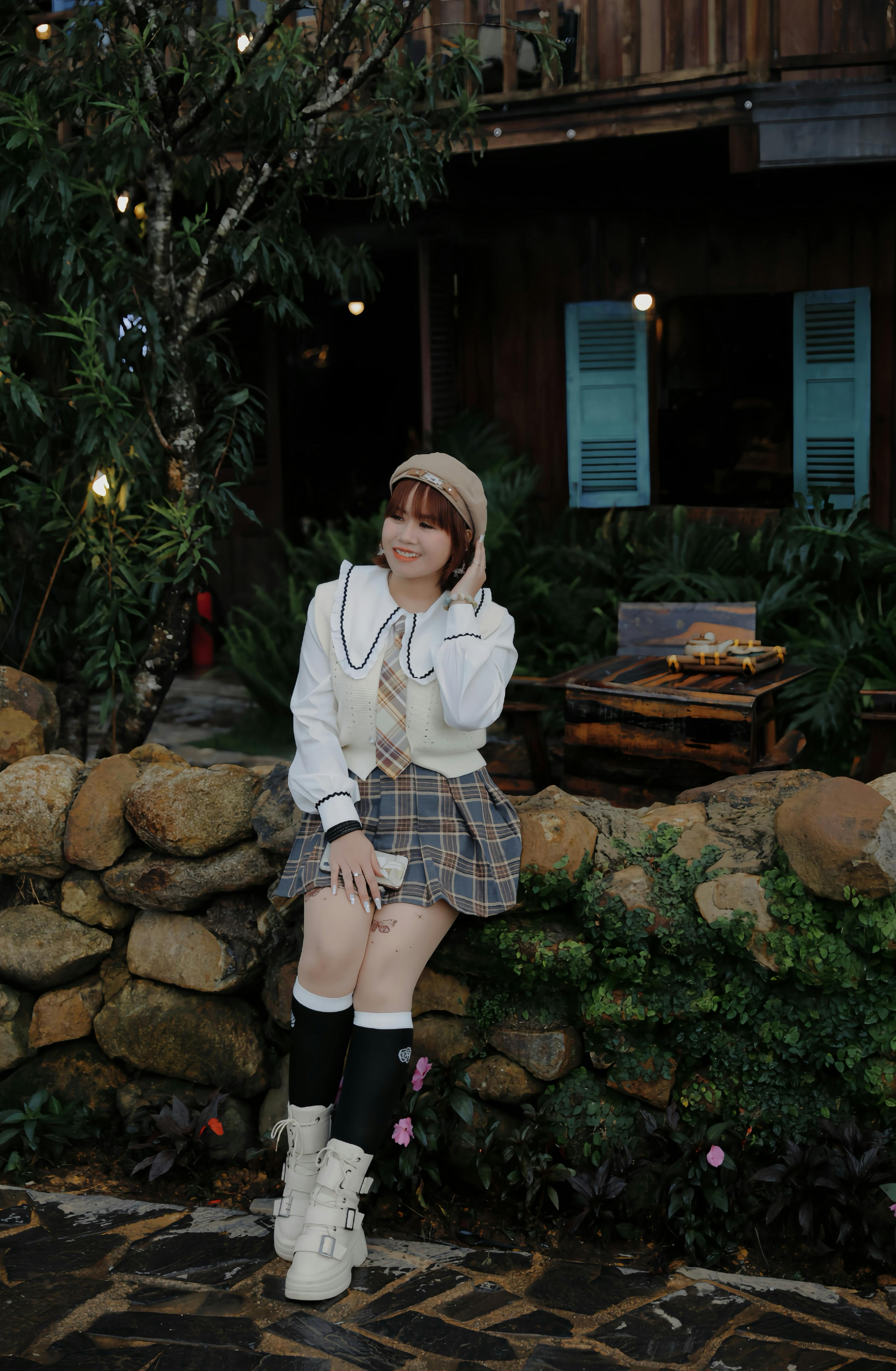 Free Young woman in fall fashion posing by a rustic stone wall outdoors. Stock Photo