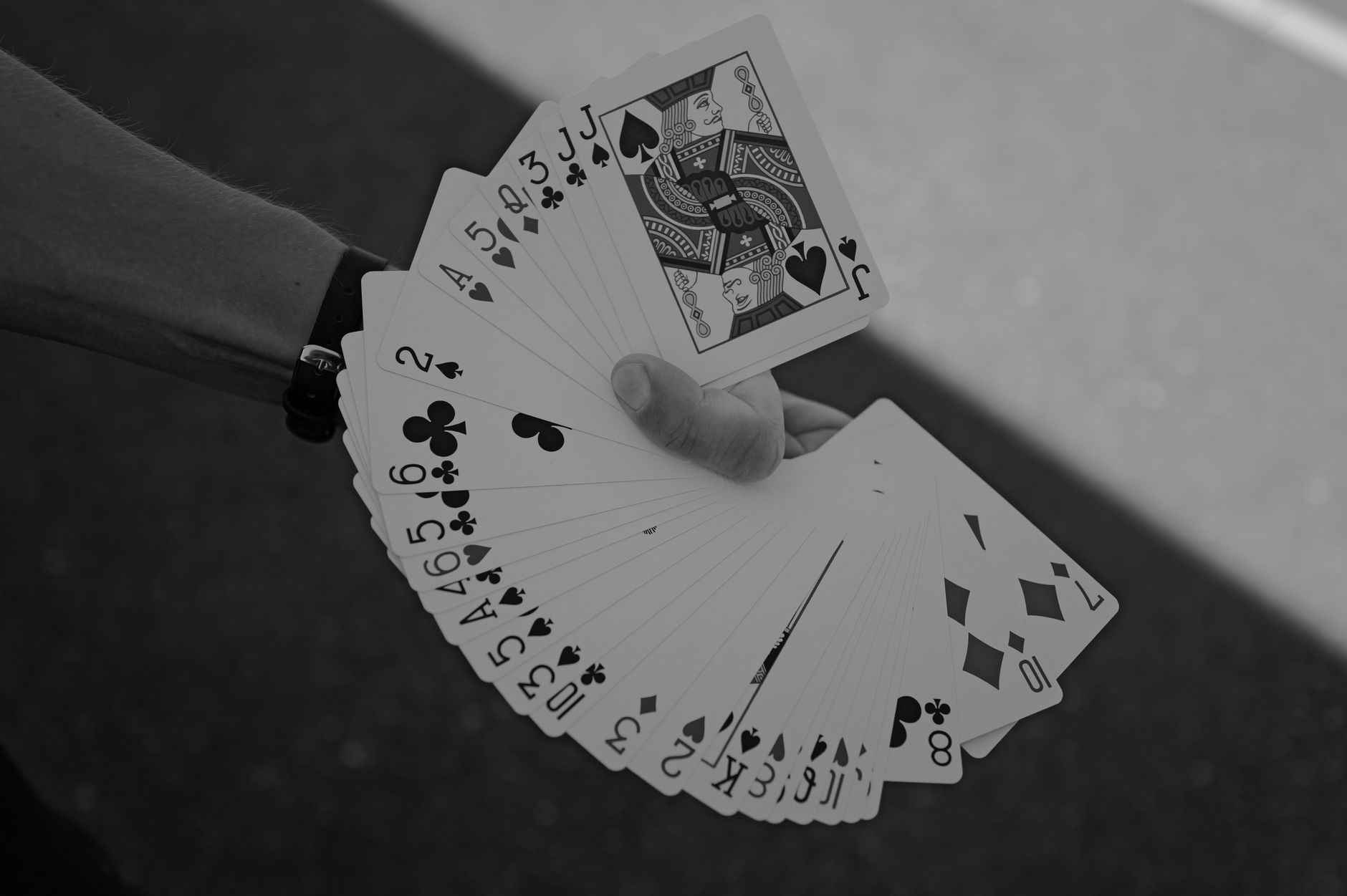 Artistic black and white photo of a hand displaying a fan of playing cards outdoors.