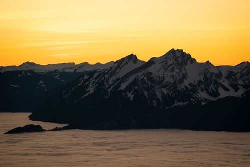 Free Dramatic view of snow-covered mountains against a vibrant orange sunset sky. Stock Photo