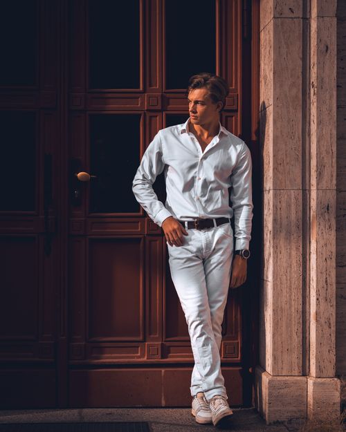 Free Fashionable young man in white outfit leaning against a wooden door, exuding classic style and confidence. Stock Photo