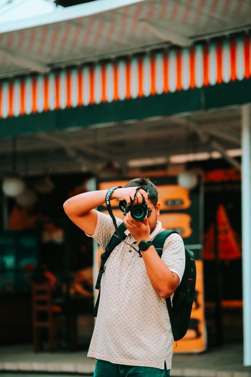 Free Man with camera photographing in an urban setting, showcasing outdoor street style. Stock Photo
