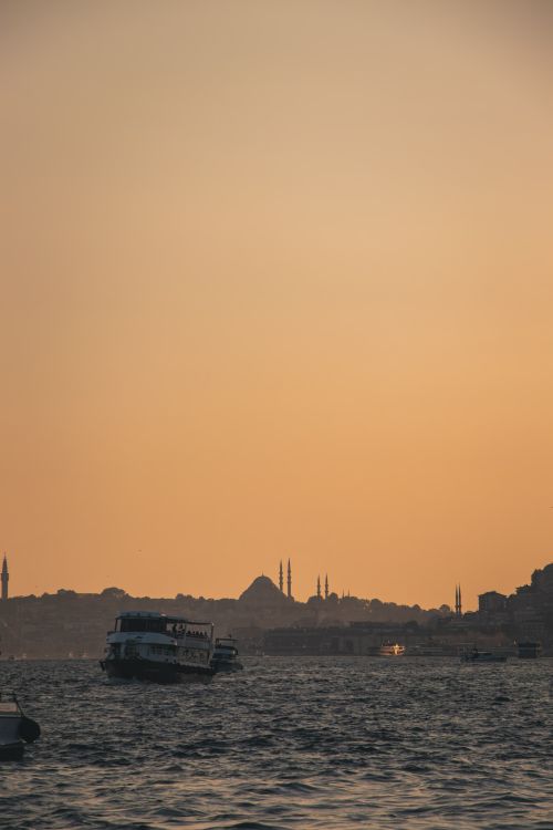 Free Tranquil view of boats on Bosphorus at sunset, with Istanbul skyline and mosques in silhouette. Stock Photo