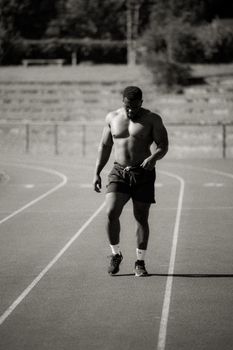 A muscular male athlete walking on a track in a black and white photograph.
