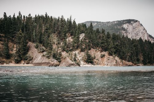 Free Serene view of lush pine forests and rocky mountains by a tranquil lake in Banff National Park. Stock Photo