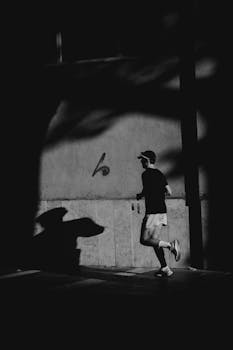 Silhouette of a runner in black and white, creating dramatic shadows on an urban street.