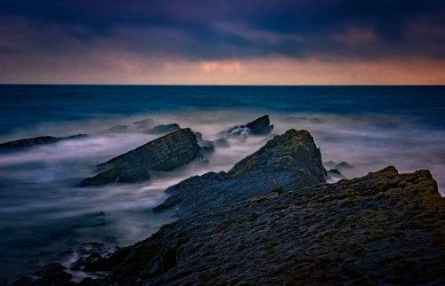 Free A breathtaking seascape featuring rocky coastline at sunset with vivid colors and waves. Stock Photo