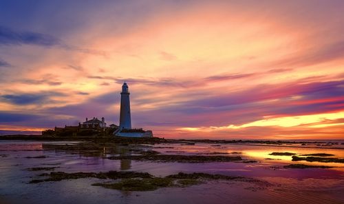 Free Vibrant sunset illuminating a coastal landscape with a lighthouse and reflecting water. Stock Photo