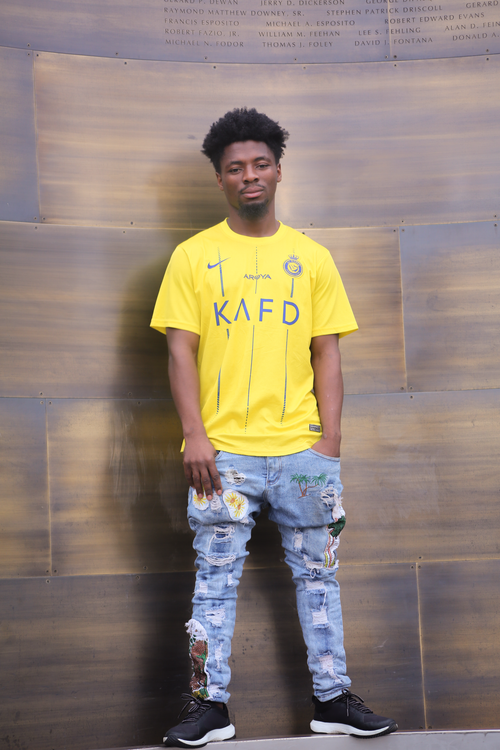 Free Stylish black man wearing a yellow soccer jersey and designer jeans poses confidently outdoors in Boston. Stock Photo
