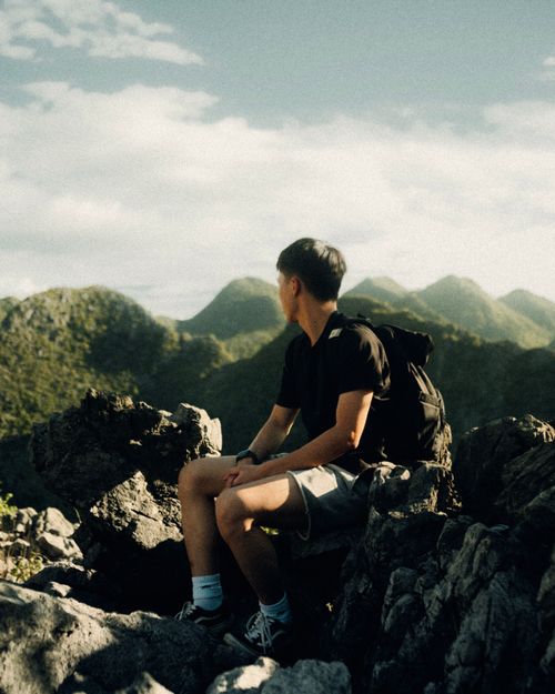 Free A man rests on rocky terrain enjoying a scenic mountain view under a clear sky. Stock Photo