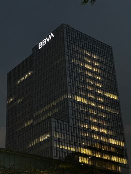 A modern office building with BBVA logo illuminated against the evening sky.